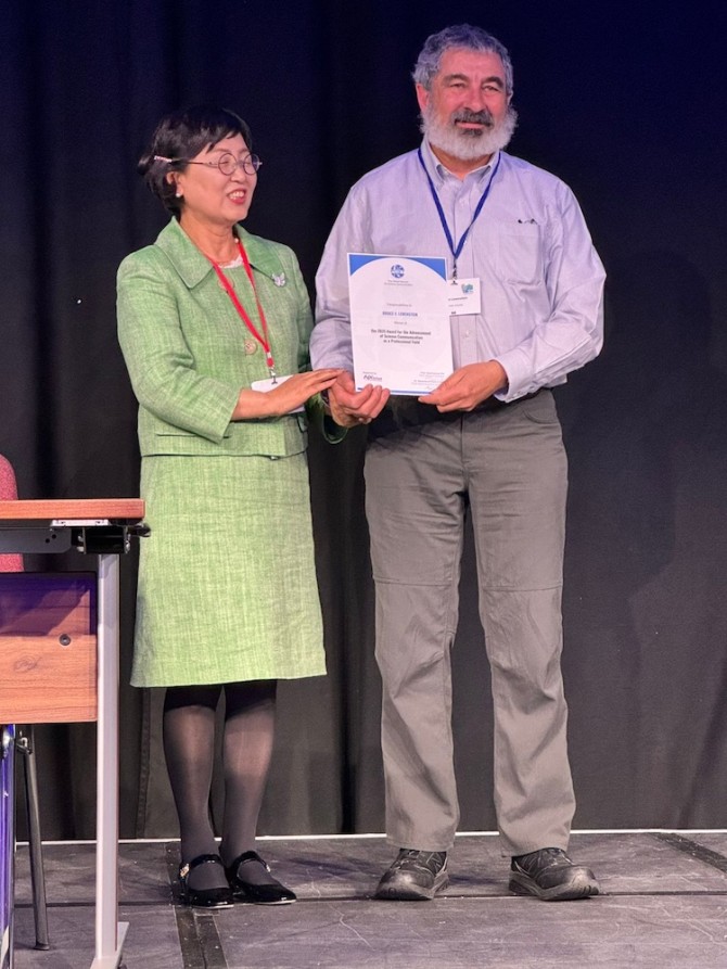 Two people standing on a stage, holding a certificate between them
