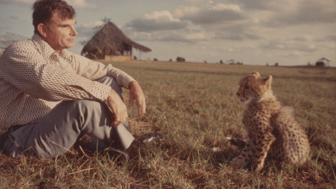 man sitting next to a cheetah cub