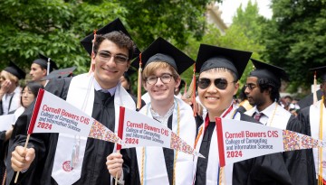 Three graduates holding Cornell Bower CIS pennants. 