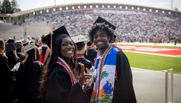 Two graduates smile at the camera in the stadium. 