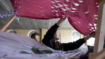 Two students draping material over the dragon's frame. 