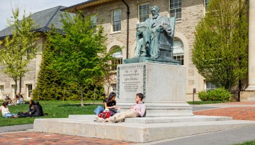 Students sit on Andrew Dickson White statue in Arts Quad.